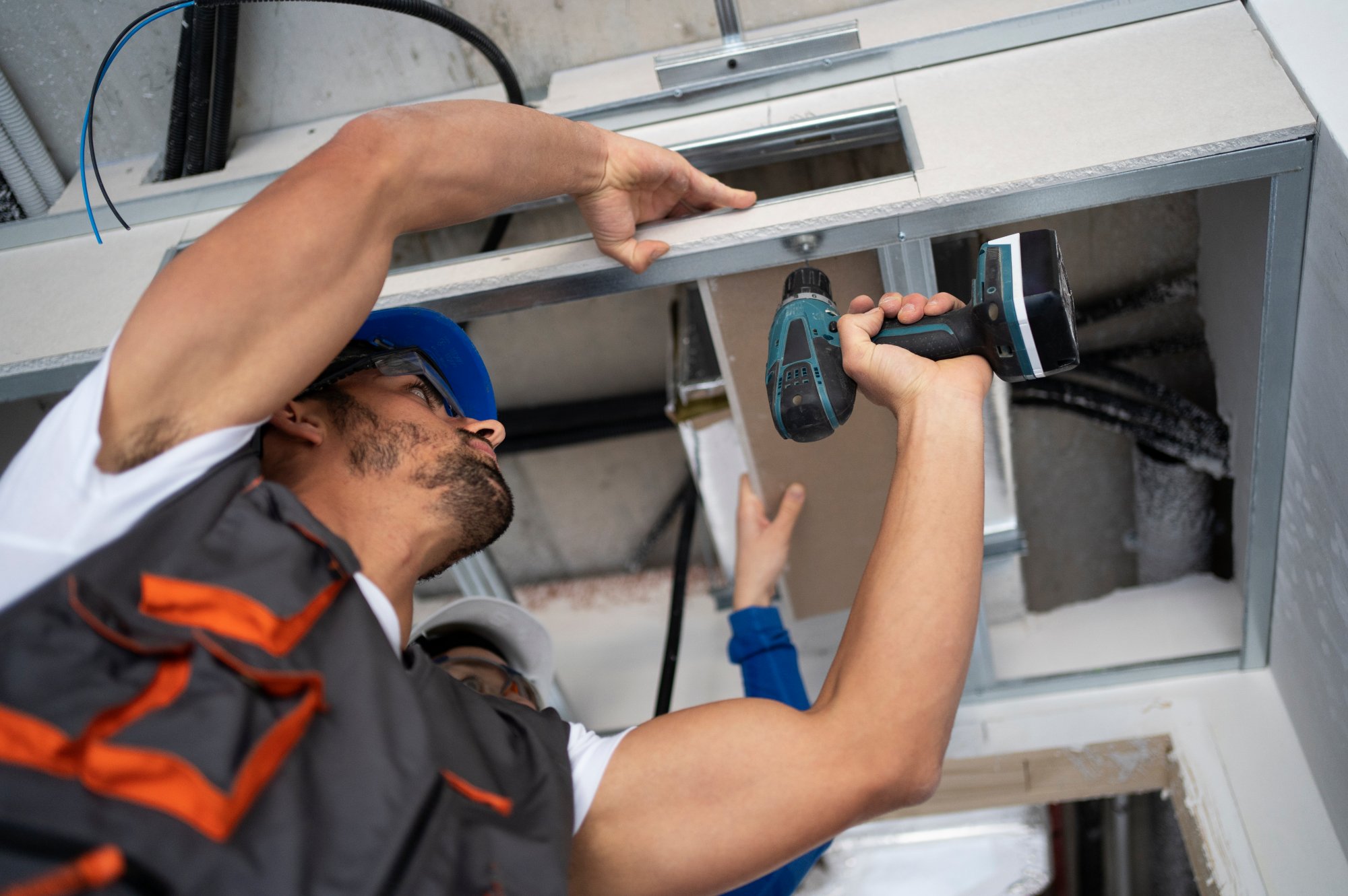 Worker installing ceiling ductwork with power drill.